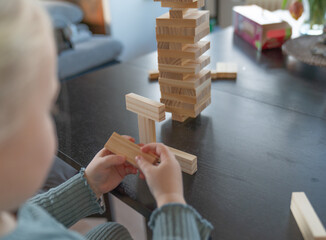 A toddler gitl builds a wooden tower on a table