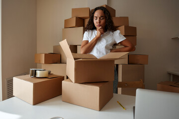 Pretty young woman in casual clothes stands at home with a postal parcel, unpacks a cardboard box, looking excited. Home delivery, shopping and online shopping concept