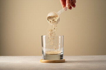 Pouring protein powder from scoop, in glass a glass. Making protein drink. - obrazy, fototapety, plakaty