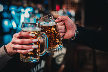 man and woman hands clinking with glasses of light beer at the pub or bar