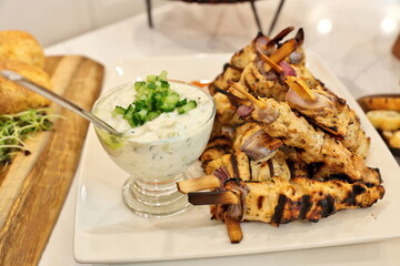 Greek chicken souvlaki skewers or kebabs piled high on a white plate with a bowl of tzatziki sauce