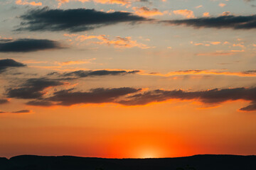 Sun hidden behind the silhouette of a mountain. Summer sunset in yellow and orange colours. The sun's rays from below beautifully illuminate the dark clouds. The beauty of nature.