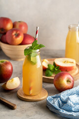 Apple juice in glass bottle, with fresh mint and red apples, wooden background. 