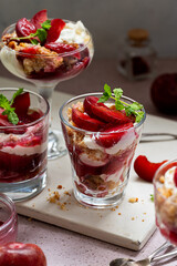 Trifles in layers with red plums and whipped cream in portioned glasses.