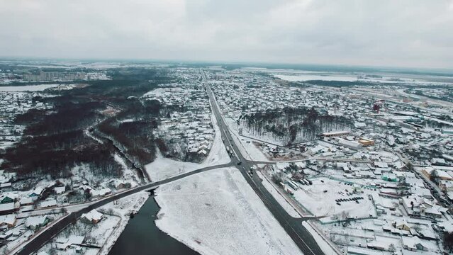 Aerial view of blocks with private houses among snow-covered fields and new microdistrict on outskirts of city