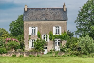 Exterior of an old house with a beautiful garden and surrounded by trees against blue cloudy sky