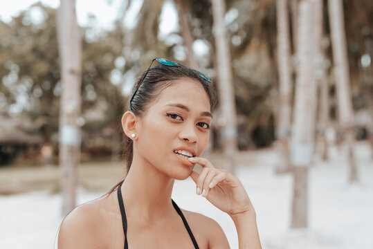 A Filipino woman bites her finger while looking flirtatiously at someone. Physical attraction concept. Outdoor scene near the beach.