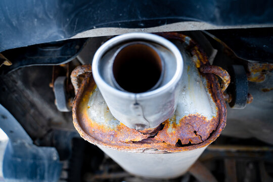 Rusty car exhaust muffler with a through hole, close-up. Corrosion on a metal exhaust pipe after winter. The reaction of salts and reagents in winter on metal parts of a car