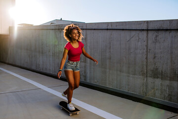 Multiracial teenage girl riding a skateboard in front of concrete wall, balancing. Side view. - Powered by Adobe