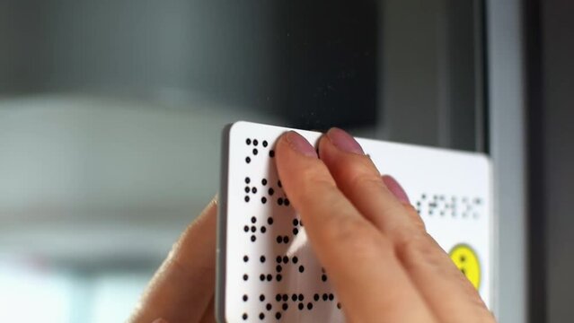 Person with blindness touches and reads with his hands the Braille text on information plate on the door of a train or bus. Close-up of fingers touching the points sign. Sightless, low vision.