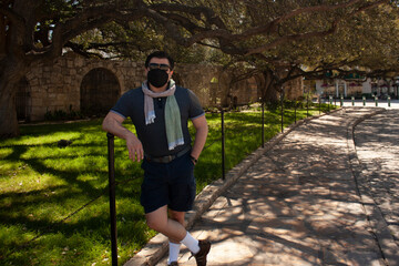 Fototapeta premium Caucasian Mexican man visitor wearing mask and sunglasses on Alamo sightseeing in San Antonio Texas on street next to the garden