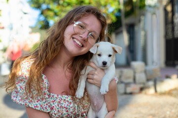 Young girl picked up a homeless dog and holding in his armson the street, a person's hand strokes...