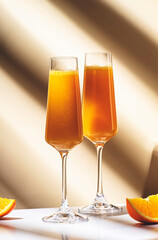 Mimosa alcohol cocktail drink with orange juice and cold dry champagne or sparkling wine in glasses. Beige background, hard light, shadow pattern