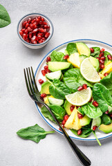 Fresh vegan salad with pineapple, spinach, avocado and pomegranate seeds, gray kitchen table, top view. Healthy eating, clean food, diet, weight loss concept