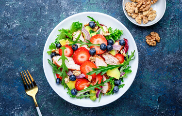 Strawberry, grilled chicken and herbs healthy salad with arugula, blueberries, avocado and walnuts, blue kitchen table. Fresh useful dish for healthy eating