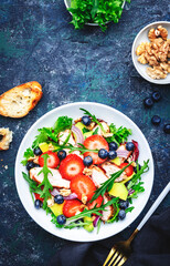 Strawberry, grilled chicken and herbs healthy salad with arugula, blueberries, avocado and walnuts, blue kitchen table. Fresh useful dish for healthy eating