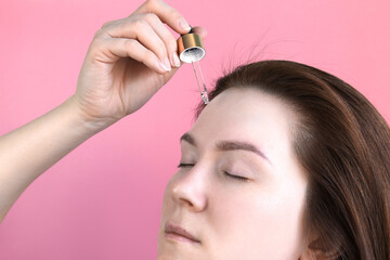 A beautiful girl applies a skin care product or vitamins or natural oils to her face with a pipette.