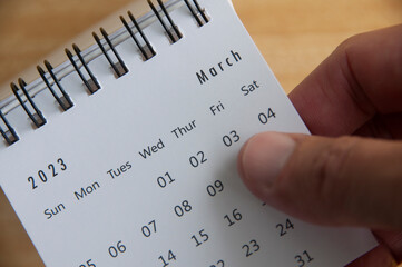 Top view of hand flipping March 2023 calendar. Calendar concept