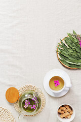 Fototapeta na wymiar Fireweed tea in white cups and transparent glass teapot, herbal hot tea from green leaves of ivan chai on textile tablecloth. Top view healthy drink and wild flowering willow-herb, tea time