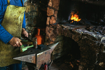 Blacksmith manually forging the molten metal on the anvil in smithy with spark fireworks, close up