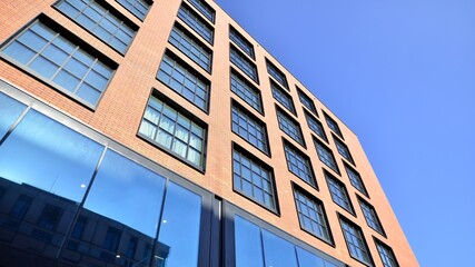 A modern corporate building in the city.  The blue sky is reflected in the buildings large glass windows. Glass facade.