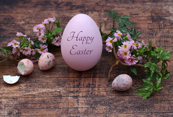 Easter greeting card: Pink Easter egg with the inscription Happy Easter with flowers and quail eggs on a rustic wooden background.