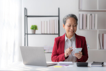 Asian senior businesswoman sitting using smartphone in the office.