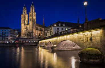 Panorama of Grossmünster church and bridge in Zürich city center during evening with street lights
