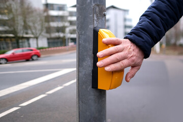 male hand presses a yellow device with a button on demand with a symbol of a man to cross the road...