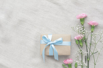 Fototapeta na wymiar Present of pink carnations, white hazel and blue ribbon on a gray tablecloth
