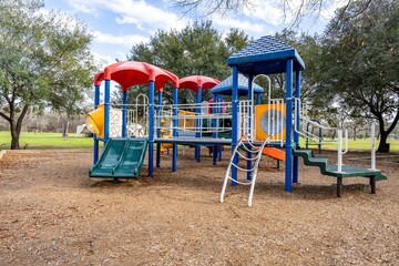 Colorful children's playground activities in a public park surrounded by trees in the daytime
