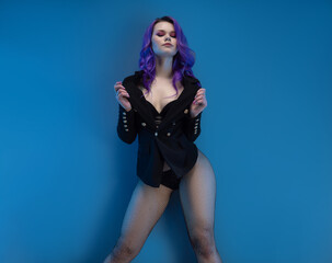 Fototapeta na wymiar sexy girl in a fancy jacket and purple hair posing erotically in her underwear against a blue background copy paste