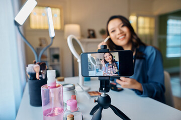 Close up of happy Asian influencer recording makeup vlog with mobile phone.