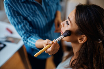 Close up of makeup artist applying blush on woman's cheek.