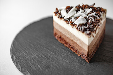 Cake three chocolate with crumb, puff meringue of light milk white and dark chocolate, on slate stone plate round, dark backgroundt