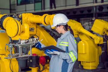 Female engineer wearing uniform and safety helmet inspecting repair parts and robotic arm monitor in factory
