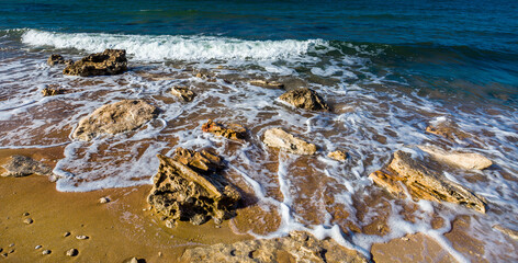 Marine surf on sandy coast with big stone, sea waves and white foam
