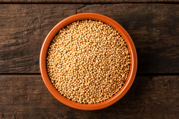 Mustard seeds in bowl on retro wooden background. Top view