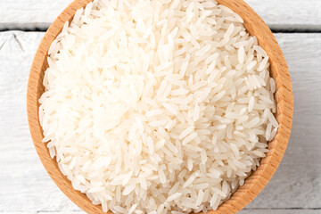 Uncooked white rice in bowl on rustic wooden table. Top view