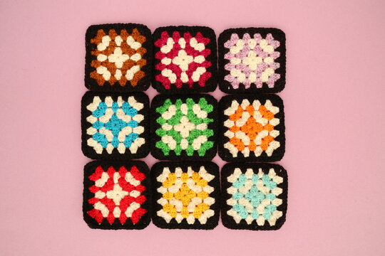 Close-up overhead view of nine crochet squares on a pink background