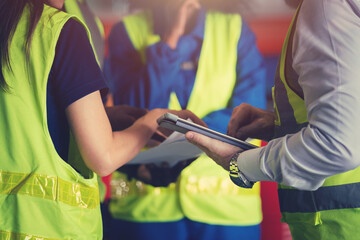 Group of diverse warehouse worker in safety suit, Project manager using blueprint and digital tablet to discussing with engineer team for work in construction industry. Teamwork and unity concept.