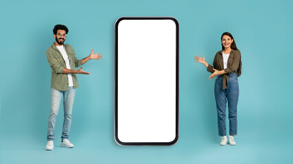 Positive mixed race couple standing by big cell phone, mockup