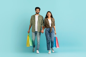 Happy multiracial young couple holding shopping bags, walking on blue