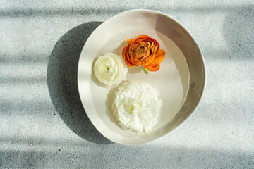 Overhead view of orange and white Ranunculus flower heads floating in a bowl of water