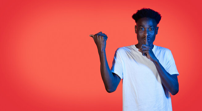 Black guy showing silence gesure and pointing at copy space