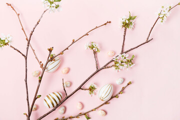 Colorful Easter eggs with cherry blossoms flat lay on pink background.