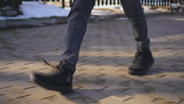 Unrecognizable man feets walks along country road near snow drifts in winter sunset rays slow motion. Man legs walking on paved way. Young people lifestyle concept