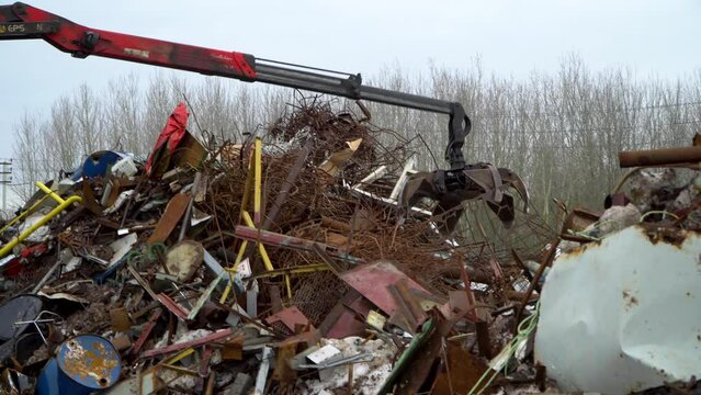 A grab loader loads industrial scrap metal for recycling. Manipulator with a hydraulic magnet crab on the background of the sky. The crane captures scrap metal.