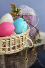 Happy Easter spring holiday. Decoration with tree branches, green leaves, bright colored eggs in a basket with hay, Easter cake on a light wooden background.