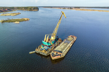 aerial view on crane extracts minerals from bottom onto huge barge in middle of lake or sea